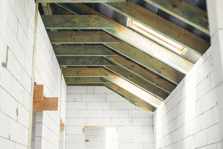 Unfinished attic wooden roof framing with vapor barrier, dormer and windows. View on timber rafters and beams on aerated concrete blocks in mansard. New modern farmhouse constructionの写真素材