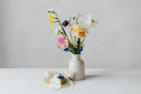 Happy womens day and Mother's day. Stylish gift box with ribbon and spring flowers on rustic white table. Beautiful daffodils and tulips gentle bouquet and present. Space for textの写真素材