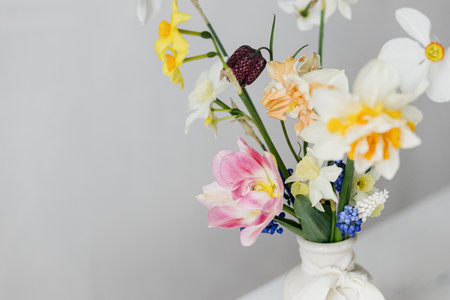 Stylish spring flowers in vase with ribbon on rustic white table. Happy womens day and Mother's day. Beautiful daffodils and tulips gentle bouquet still life. Space for textの写真素材