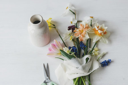 Stylish spring flowers with ribbon and scissors still life. Beautiful daffodils and tulips gentle bouquet on rustic white table flat lay. Happy womens day and Mother's dayの写真素材