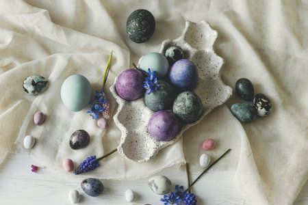 Happy Easter! Stylish easter eggs in modern tray and spring flowers on linen cloth on rustic white table. Easter simple banner, space for text. Natural painted marble and purple eggs still lifeの写真素材