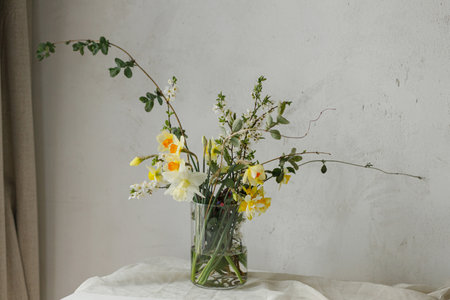 Stylish spring flowers bouquet on rustic table in rural room. Beautiful daffodils, cherry bloom and greenery composition in glass vase. Easter modern simple decorの写真素材