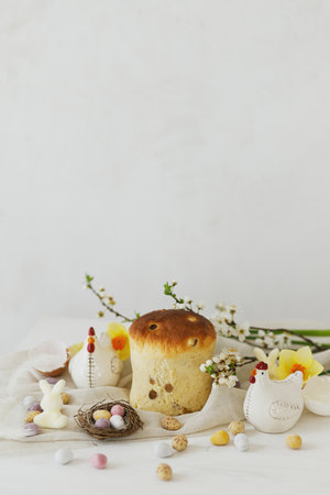 Colorful easter chocolate eggs in nest, spring flowers, traditional bread  composition on rustic white wooden table. Space for text. Happy Easter! Seasons greetingsの写真素材
