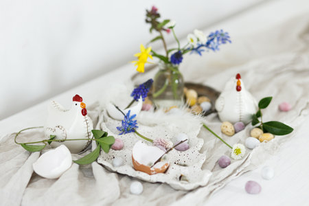 Stylish easter chocolate eggs, spring flowers, chicken figurines and linen cloth on rustic wooden table. Space for text. Easter modern simple decoration. Happy Easter!の写真素材
