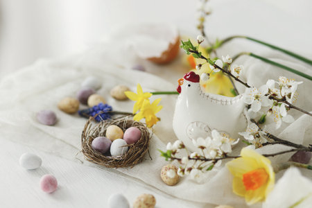 Easter still life. Colorful easter chocolate eggs in nest, spring flowers, chicken figurine composition on white wooden table. Space for text. Happy Easter! Seasons greetingsの写真素材