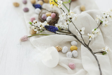 Happy Easter! Stylish easter chocolate eggs, spring flowers, feathers and linen cloth on white rustic wooden table. Easter modern simple banner, space for text. Seasons greetingsの写真素材