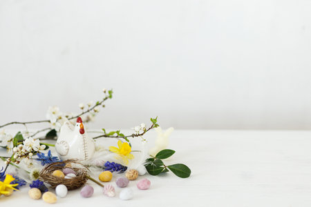 Easter still life. Colorful easter chocolate eggs in nest, spring flowers, chicken figurine composition on white wooden table. Space for text. Happy Easter! Seasons greetingsの写真素材