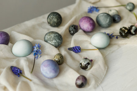 Stylish easter eggs, gentle spring flowers and linen cloth on rustic white table.Holiday banner. Happy Easter! Natural painted marble and purple eggsの写真素材