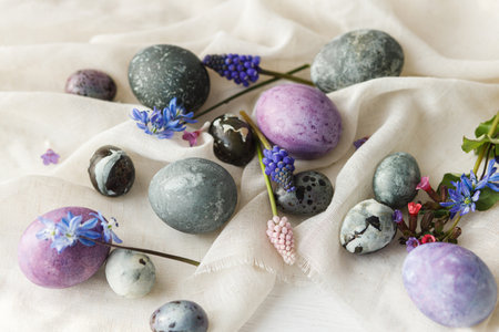 Happy Easter! Stylish easter eggs and spring flowers on linen cloth on rustic white table. Easter modern simple banner, space for text. Natural painted marble and purple eggs still lifeの写真素材