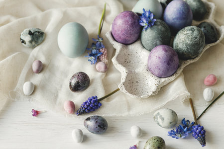 Happy Easter! Stylish easter eggs in modern tray and spring flowers on linen cloth on rustic white table. Easter simple banner, space for text. Natural painted marble and purple eggs still lifeの写真素材