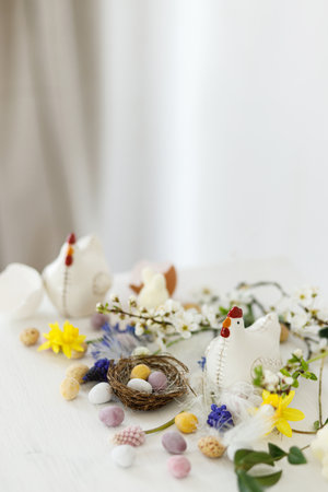 Happy Easter! Stylish easter chocolate eggs in nest, spring flowers, chicken figurine on white rustic wooden table. Easter modern simple banner, space for text. Seasons greetingsの写真素材