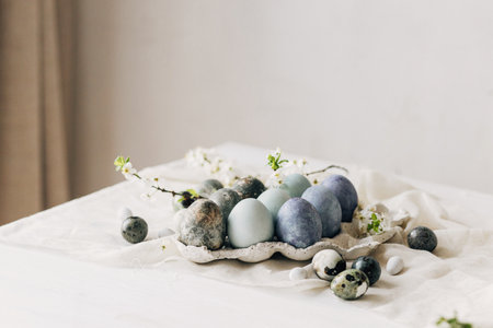 Stylish Easter eggs and spring flowers on rustic table. Happy Easter! Natural dye marble and blue eggs in tray and cherry blossoms. Happy Easter! Holiday minimal still lifeの写真素材