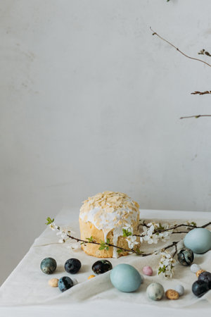 Stylish easter eggs, panettone and spring flowers on linen cloth on rustic table. Natural dye eggs and cherry blossom, festive minimal still life. Happy Easter!の写真素材