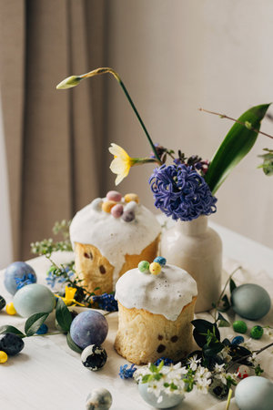 Stylish easter eggs, panettone, spring flowers and chocolate eggs on rustic wooden table. Natural...