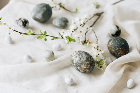 Happy Easter! Stylish easter eggs and spring flowers on linen rustic table. Natural painted marble eggs and cherry blooms. Modern minimal still lifeの写真素材