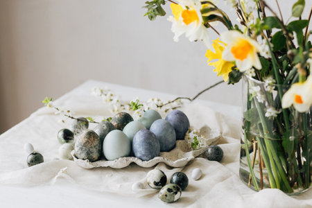 Stylish Easter eggs and spring flowers on rustic table. Happy Easter! Natural dye marble and blue...
