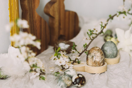 Happy Easter! Stylish easter eggs, wooden bunnies, cherry blossom and candle on rustic table. Modern...