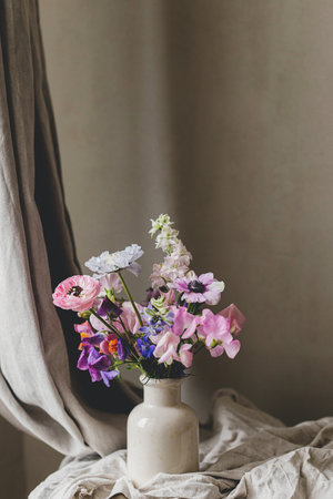 Stylish bouquet on rustic linen background. Beautiful colorful anemone, ranunculus, lathyrus scabiosa in vase. Summer flowers, floral moody still life. Space for textの写真素材