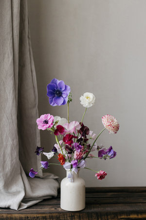 Summer flowers in vase, rustic still life. Beautiful colorful anemone, ranunculus, lathyrus on aged wooden bench with linen curtains. Floral moody wallpaper. Space for textの写真素材