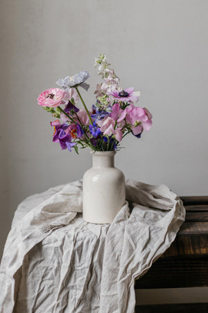 Summer flowers in vase, rustic moody still life. Beautiful colorful anemone, ranunculus, lathyrus, scabiosa on aged bench with linen cloth. Floral moody wallpaper. Space for textの写真素材