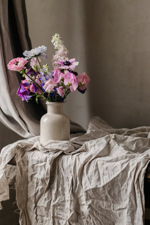 Stylish bouquet on rustic linen background. Beautiful colorful anemone, ranunculus, lathyrus scabiosa in vase. Summer flowers, floral moody still life. Space for textの写真素材