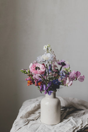 Stylish bouquet on rustic linen background. Beautiful colorful anemone, ranunculus, lathyrus scabiosa in vase. Summer flowers, floral moody still life. Space for textの写真素材