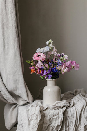 Summer flowers in vase, rustic moody still life. Beautiful colorful anemone, ranunculus, lathyrus, scabiosa on aged bench with linen cloth. Floral moody wallpaper. Space for textの写真素材