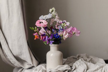 Summer flowers in vase, rustic moody still life. Beautiful colorful anemone, ranunculus, lathyrus, scabiosa on aged bench with linen cloth. Floral moody wallpaper. Space for textの写真素材