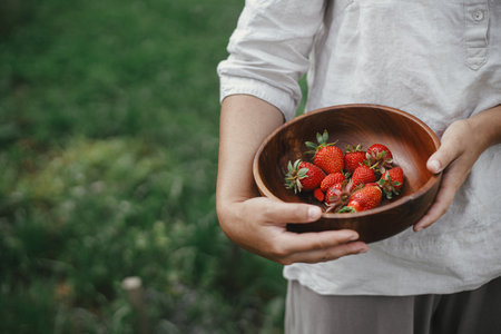 Woman holding wooden bowl with strawberries close up. Gathering fresh natural berries in urban organic garden. Homestead lifestyleの写真素材