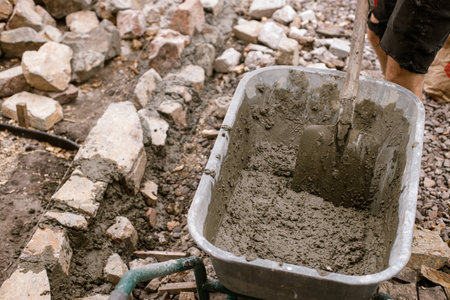 Wheelbarrow with concrete and stones for pathway in cottage garden. Close up of spade with cement, making edge for path in modern urban gardenの写真素材