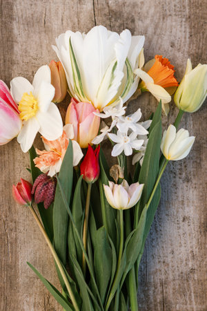 Beautiful bouquet rustic flat lay on aged wooden background. Spring daffodils and tulips top view, floral rural template. Growing spring flowers. Mothers day cardの写真素材