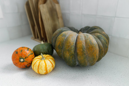 Pumpkins and wooden cutting board on modern kitchen countertop. Autumn harvest and pumpkin recipes. Space for text. Thanksgiving home made foodの写真素材