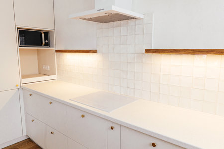 Modern minimal kitchen design. Stylish white electric cooker, kitchen cabinets with brass knobs, granite counter, wooden shelves and appliances in new scandinavian house.  Modern kitchen interiorの写真素材