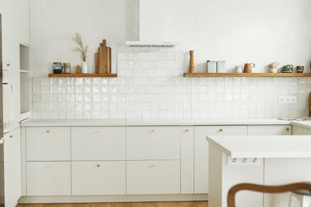 Modern minimal kitchen design. Stylish white kitchen cabinets with brass knobs, granite countertop, appliances and utensils on wooden shelves in new scandinavian house. Modern kitchen interior.の写真素材
