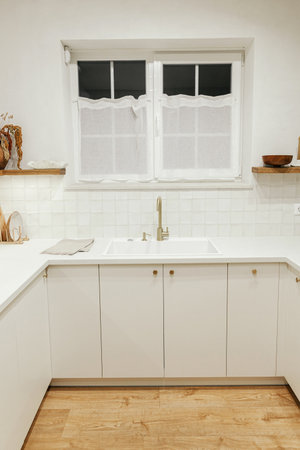 Modern kitchen interior. Stylish white kitchen cabinets, brass faucet and granite sink, wooden shelves with utensils and evening light  in new scandinavian house. Modern minimal kitchen designの写真素材