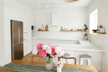 Modern kitchen interior. Beautiful peonies in vase on wooden table and stylish white kitchen with appliances in new scandinavian house. Minimal kitchen design and summer floral arrangementの写真素材