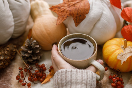 Hello autumn. Hand in sweater holding warm cup of tea and pumpkins, fall leaves and candle on windowsill. Autumn hygge, ugc concept. Happy Thanksgivingの写真素材