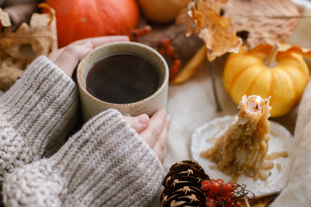 Cozy autumn. Hands in sweater holding warm cup of tea and pumpkins, fall leaves and candle on window sill. Autumn hygge. Happy Thanksgivingの写真素材