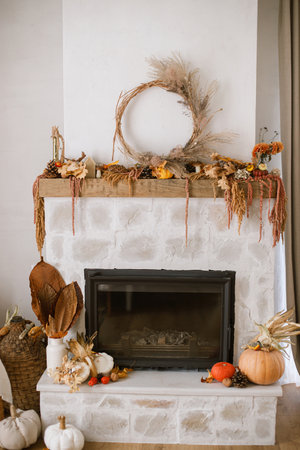 Stylish decoration of fireplace with pumpkins, wreath, autumn leaves, nuts, candle on rustic wood in modern farmhouse living room. Autumn fireplace mantel. Thanksgiving and Halloweenの写真素材