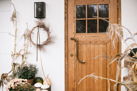 Fall decor of farm house entrance. Rustic wreath, pumpkins, moms flowers, corn at front door. Thanksgiving and Halloween. Rural autumn decorationの写真素材
