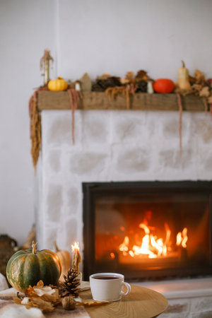 Warm cup of tea, pumpkin, autumn leaves on wooden table on background of burning fireplace. Cozy autumn still life. Thanksgiving and Halloween. Fall hyggeの写真素材