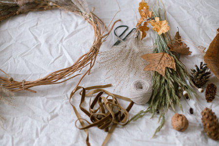 Making stylish autumn wreath. Dried grass, herbs, leaves, ribbon and scissors on rustic table. Details of fall decor and arrangement in home. Thanksgiving and Halloweenの写真素材