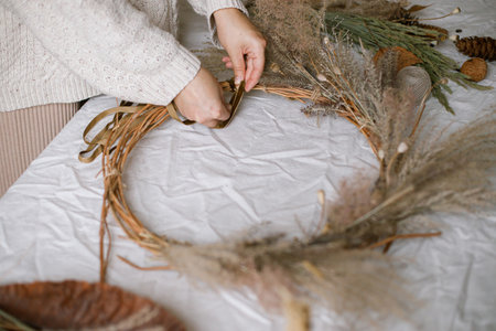 Hands holding dried grass, herbs, leaves, ribbon and scissors on rustic table. Making stylish autumn wreath. Fall decor and arrangement in home. Thanksgiving and Halloweenの写真素材