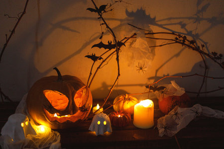 Happy Halloween! Spooky Jack o lantern pumpkin, glowing ghosts, lights, spiders and bats in dark. Atmospheric halloween decor, festive autumn still life. Trick or treatの写真素材