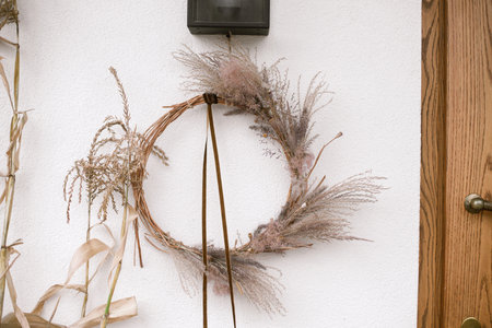 Stylish autumn wreath at wooden doors. Fall decor of farm house entrance. Rustic wreath with dried grass, herbs and ribbon. Thanksgiving and Halloweenの写真素材