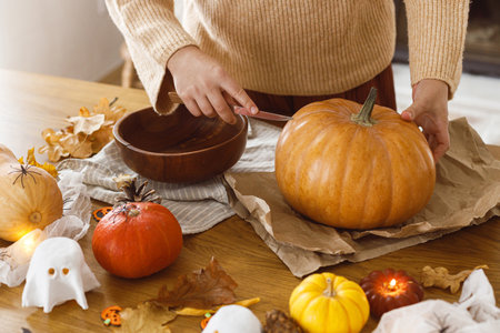 Carving halloween pumpkin. Woman holding pumpkin and knife on table with ghosts and spiders in living room. Carve a pumpkin, halloween preparation. Making halloween decorationsの写真素材