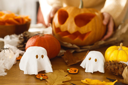 Happy halloween! Making jack o lantern. Woman carving halloween pumpkin on table with ghosts and spiders, halloween preparationの写真素材