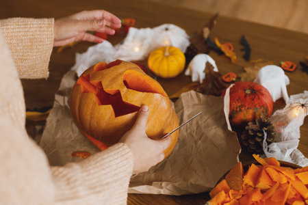 Carving halloween pumpkin. Woman holding pumpkin and knife on table with ghosts and spiders. Carve a jack o lantern, halloween preparation. Making halloween decorationsの写真素材