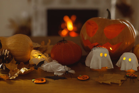 Happy Halloween! Glowing Jack o lantern, glowing ghosts, pumpkin and spiders on table in evening. Spooky atmospheric halloween decorations, space for textの写真素材