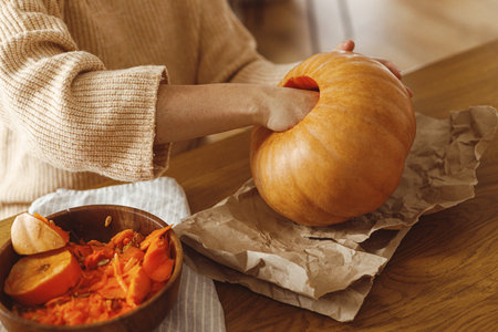 Carving halloween pumpkin. Woman holding pumpkin and gutting on table with ghosts and spiders in living room. Carve a pumpkin, halloween preparation. Making halloween decorationsの写真素材